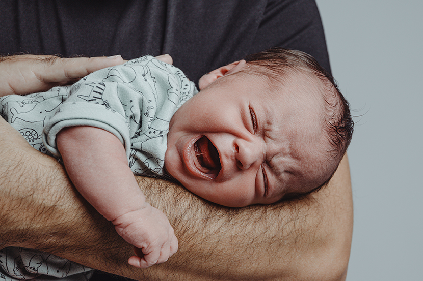 newborn on his father's arm screams crying with expression of suffering