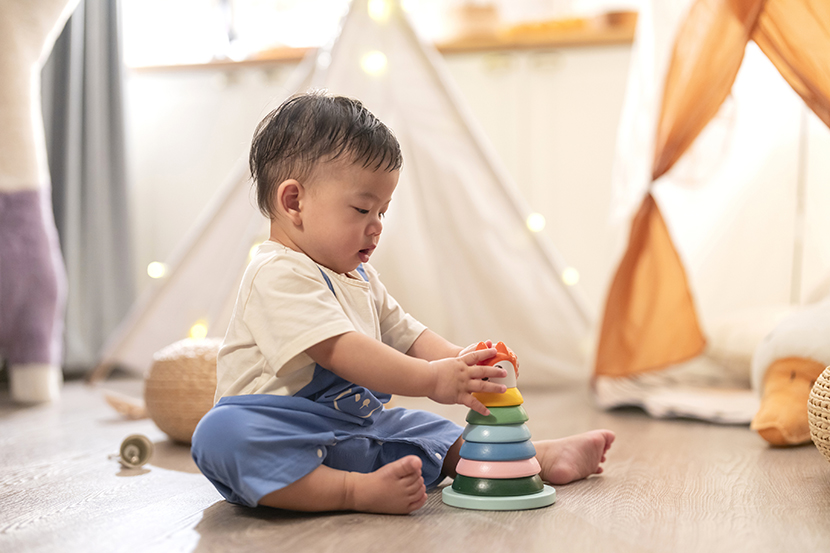 Happiness cutre asian boy 8-12 month playing sit relax and play wooden stack ring balance pratice hand muscle control smart colourful toy on carpet in living room at night home interior background