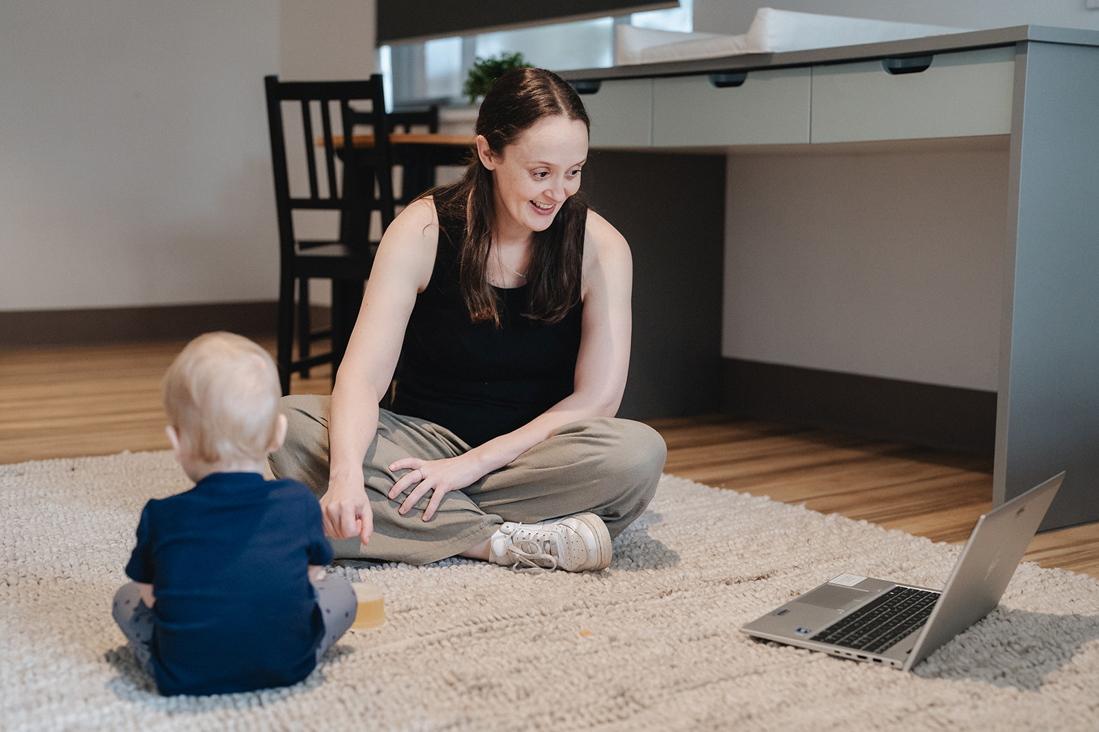 A mum and her baby sitting on the floor involved in a Karitane webinar via a laptop